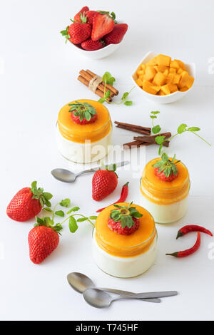 Traditionelle italienische süßes Dessert Panna cotta mit Mango Gelee mit Hauch von red hot chili Piri-Piri in Töpfen auf weissem Holztisch und embellis serviert. Stockfoto