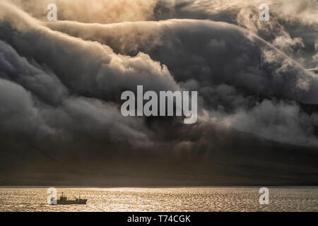 Fischereifahrzeug mit dramatischen Wolken über die Berge fließt; Ost: Fjorde, Island Stockfoto