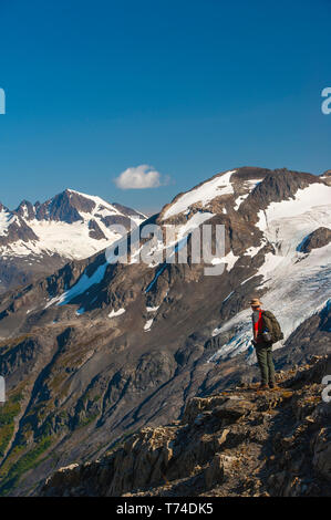 Der Kenai Fjords National Park, ein Mann, der in der Nähe des Harding Icefield Trail mit den Kenai Mountains und einem namenlosen hängenden Gletscher... Stockfoto