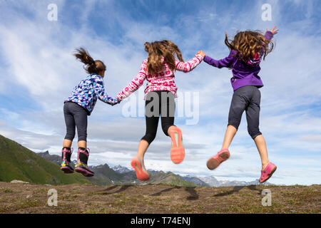 Drei junge Schwestern springen und halten sich an den Händen in der Talkeetna Berge, Hatcher Pass, Alaska, Vereinigte Staaten von Amerika Stockfoto