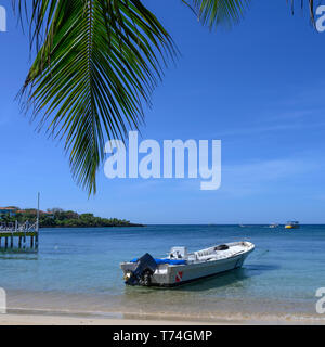 Boot auf den Strand entlang der West End von Roatan mit Blick auf die Küste und den blauen Himmel gegen den Horizont; Roatan, Bay Islands, Honduras Stockfoto