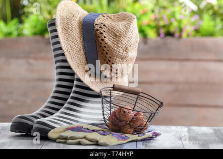 Zusammensetzung mit Gummistiefeln und Blumenzwiebeln auf hölzernen Tisch im Garten Stockfoto
