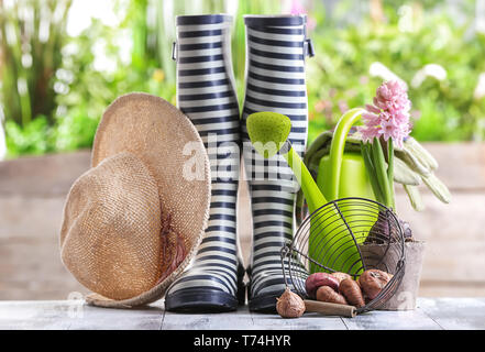 Zusammensetzung mit Gummistiefeln, Blumenzwiebeln und Gießkanne auf hölzernen Tisch im Garten Stockfoto