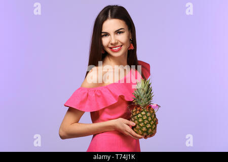 Attraktive junge Frau mit Ananas mit Sonnenbrille auf farbigen Hintergrund Stockfoto