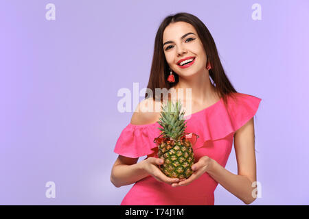 Attraktive junge Frau mit Ananas mit Sonnenbrille auf farbigen Hintergrund Stockfoto