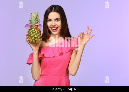 Attraktive junge Frau mit Ananas mit Sonnenbrille auf farbigen Hintergrund Stockfoto