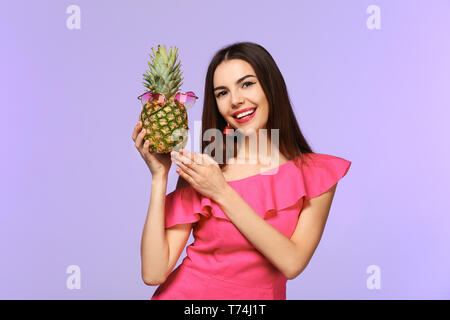 Attraktive junge Frau mit Ananas mit Sonnenbrille auf farbigen Hintergrund Stockfoto