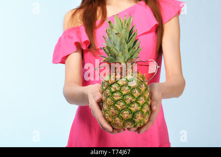 Junge Frau mit Ananas mit Sonnenbrille auf farbigen Hintergrund Stockfoto