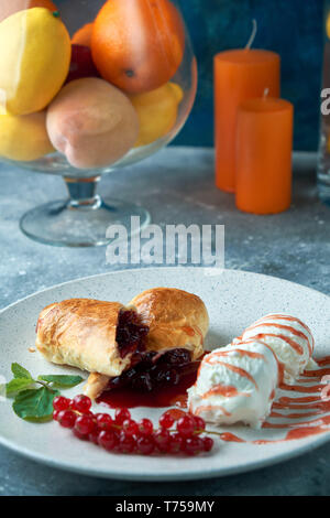 In Scheiben geschnittene Hausgemachte berry Strudel mit frischen rote Johannisbeere Beeren und Puderzucker auf einem alten Hintergrund auf einer Platte mit Eis pic serviert. Stockfoto