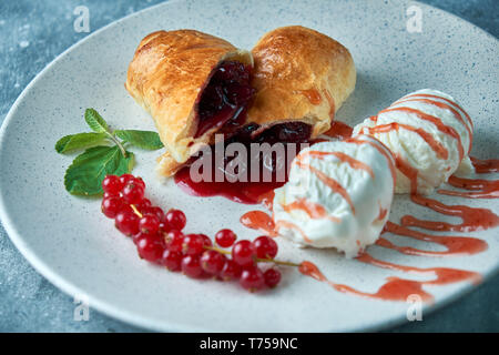 In Scheiben geschnittene Hausgemachte berry Strudel mit frischen rote Johannisbeere Beeren und Puderzucker auf einem alten Hintergrund auf einer Platte mit Eis pic serviert. Stockfoto