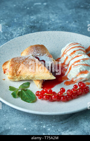 In Scheiben geschnittene Hausgemachte berry Strudel mit frischen rote Johannisbeere Beeren und Puderzucker auf einem alten Hintergrund auf einer Platte mit Eis pic serviert. Stockfoto