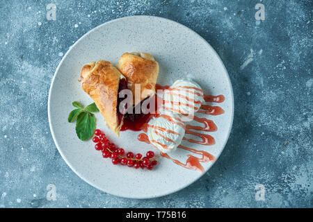 In Scheiben geschnittene Hausgemachte berry Strudel mit frischen rote Johannisbeere Beeren und Puderzucker auf einem alten Hintergrund auf einer Platte mit Eis pic serviert. Stockfoto