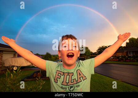 Ein kleiner Junge steht mit ausgebreiteten Armen wie ein Regenbogen über eine regionale New South Wales vorort Formen. Stockfoto