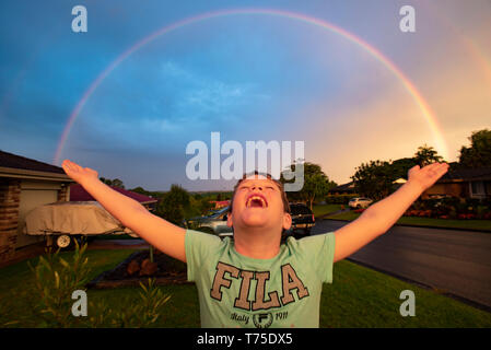 Ein kleiner Junge steht mit ausgebreiteten Armen wie ein Regenbogen über eine regionale New South Wales vorort Formen. Stockfoto