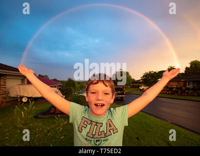 Ein kleiner Junge steht mit ausgebreiteten Armen wie ein Regenbogen über eine regionale New South Wales vorort Formen. Stockfoto