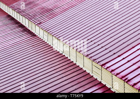 Detailansicht einer Dach aus rot gefärbten Blechen. Eine diagonale Überhang gibt einen 3-dimensionalen Eindruck. Stockfoto