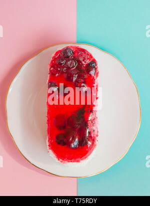 Einen schönen Kuchen mit roten Preiselbeere Sahnehäubchen auf eine weiße Platte, Rosa und Blau pastell Hintergrund Blick auf der Oberseite. Stockfoto