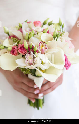 Rosa Rosen mit weißen calla, Orchideen und eustoma in einem schönen Brautstrauß, in den Händen eines unkenntlich Braut Stockfoto