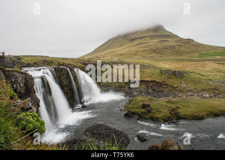 Lange Exposition von Kirkjufellsfoss mit Kirkjufell Berg im Hintergrund, verdeckt von Nebel (Island) Stockfoto