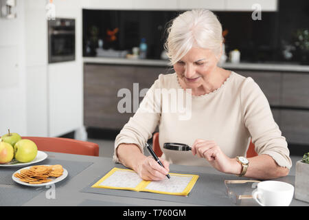 Ältere Frau genießt das Lösen eines Kreuzworträtsels zu Hause Stockfoto