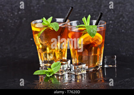 Zwei Gläser mit kaltem traditionelle Eistee mit Zitrone, Minze und Eiswürfel auf nassen schwarzen Hintergrund. Stockfoto