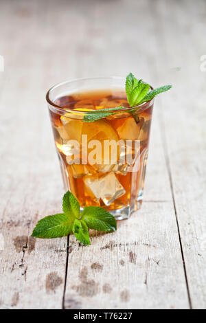 Traditionelle Eistee mit Zitrone, Minze und Eis im Glas auf rustikalen Holztisch Hintergrund. Stockfoto