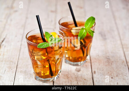 Traditionelle Eistee mit Zitrone, Minze und Eiswürfel in zwei Gläser auf rustikalen Holztisch Hintergrund. Stockfoto