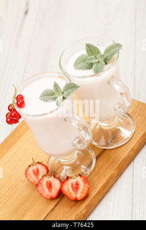Zwei Gläser köstliche Erdbeere Joghurt mit Minze und frischen Erdbeeren auf Holz Schneidebrett. Stockfoto