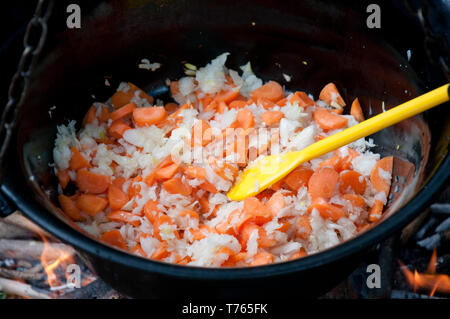 Köstliche Mahlzeit ist das Braten von Zwiebeln und Karotten in großen Wasserkocher aus Metall, mit gelben Plastiklöffel outdoor Close up Stockfoto