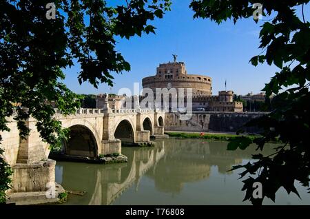 Blick durch die Bäume auf der Ponte Sant'Angelo und dem Castel Sant'Angelo über den Tiber in Rom unter einem klaren blauen Himmel, mit einer Reflexion im Wasser Stockfoto