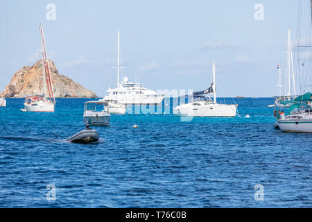 Eine Person, die ein kleines Beiboot in der Nähe der größeren Boote in den Hafen von Gustavia in St. Barts Stockfoto