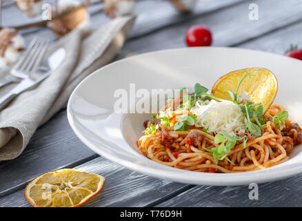 Klassische italienische Bolognese Pasta, mit microgreen, geriebenem Parmesan und einem Stück trockenen orange auf dem Tisch an einem sonnigen Tag eingerichtet Stockfoto