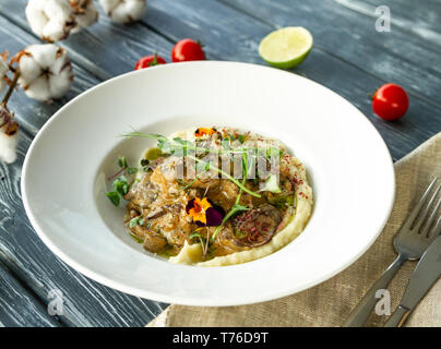 Hühnerleber in einer cremigen Sauce mit Pilzen und Kartoffelpüree auf einem Tisch mit einem Zweig von Baumwolle, Tomaten und Limettensaft Stockfoto