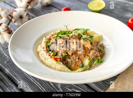 Hühnerleber in einer cremigen Sauce mit Pilzen und Kartoffelpüree auf einem Tisch mit einem Zweig von Baumwolle, Tomaten und Limettensaft Stockfoto