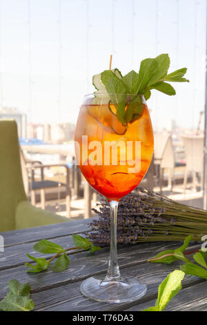 Erfrischende orange Cocktail mit Gurke und Minze im Glas auf einem Tisch vor dem Hintergrund des Fensters Stockfoto