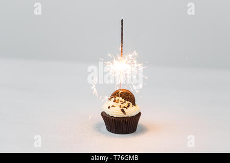 Essen, Party und Urlaub Konzept - Geburtstag Cupcake mit Wunderkerzen auf weißem Hintergrund Stockfoto