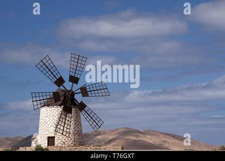 Isolierte traditionelle Windmühle (Molino de Tefia) in der Nähe von La Olivia in trockenen trockenen Hügellandschaft gegen den blauen Himmel mit Wolken cumulus, Fuerteventura, Kanarische Inseln Stockfoto