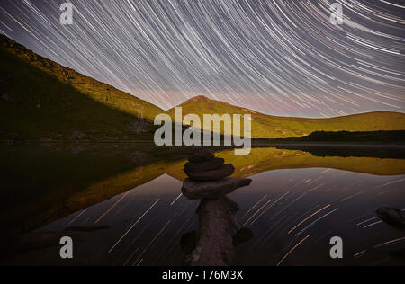 Magische Nacht Landschaft mit Bergen, See und erstaunliche Sternenhimmel, Sterne Wanderwege in den Nachthimmel, Pyramide von Steinen. Nesamovyte Chornogora, See. Carpa Stockfoto