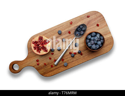 Heidelbeeren, Granatapfel mit einem silbernen Löffel auf Holz Schneidebrett, auf weißem Hintergrund Stockfoto