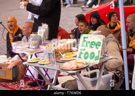 Hare Krishna Mitglieder singen und spielen auf der Straße mit Vorzeichen bietet kostenloses Essen. Stockfoto