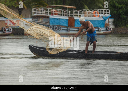 Man steht auf langen einbaum in den Untiefen der Jungle River, der Trieb einem Fischernetz mit nativen Haus Boot im Hintergrund Stockfoto