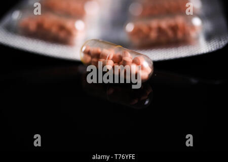 Makro Nahaufnahme der Kapsel Pillen in Silber blister Paket und einem isolierten Kapsel mit schwarzen reflektierenden Hintergrund. Transparente Hülle Perlen angezeigt Stockfoto