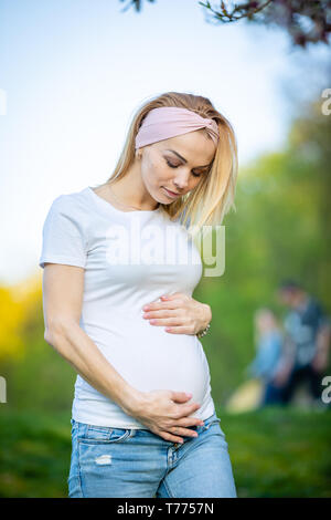 Portrait eines glücklichen und stolzen schwangere junge Frau auf ihrem Bauch im Park bei Sonnenaufgang suchen, neues Leben Konzept Stockfoto