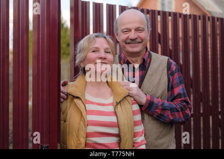 Senior Paar stehend durch Zaun in Yard lächelnd. Stockfoto