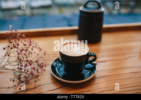 Bei einer Tasse frisch gebrühten Cappuccino Kaffee auf einem Holztisch Stockfoto