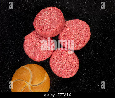 Frische rohe prime Black Angus Beef Burger Frikadellen und Brot Brötchen auf schwarzem Stein. Stockfoto