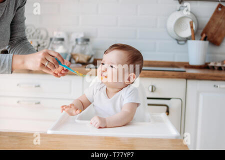 Charmantes kleines Baby Boy 6-8 Monate will nicht zuerst essen Kürbis vom Löffel mit Mama zu Hause essen Stockfoto