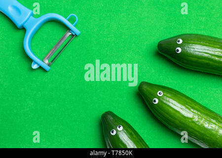 Gurken Konzept mit kopieren. Lustige Gurken mit Augen met Schälmesser. Vorbereitung salat Zutaten. Startseite flache Ansicht, grünen Hintergrund. Stockfoto