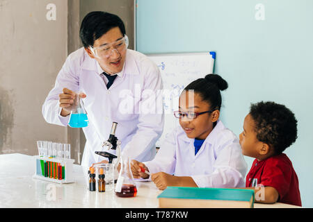 Junge Asiatische Wissenschaftler Glas Rohr Kolben und Lehre zwei Afrikanische Amerikanische gemischte Kinder in Chemie Labor Experiment in der Wissenschaft Klassenzimmer Stockfoto