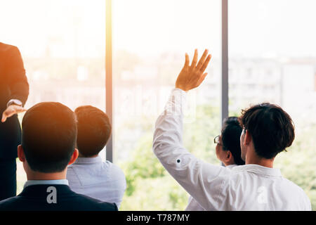 Rückansicht des Kerl in Shirt heben die Hand und Fragen stellen beim Sitzen inmitten der Kollegen während der Konferenz im Amt Stockfoto